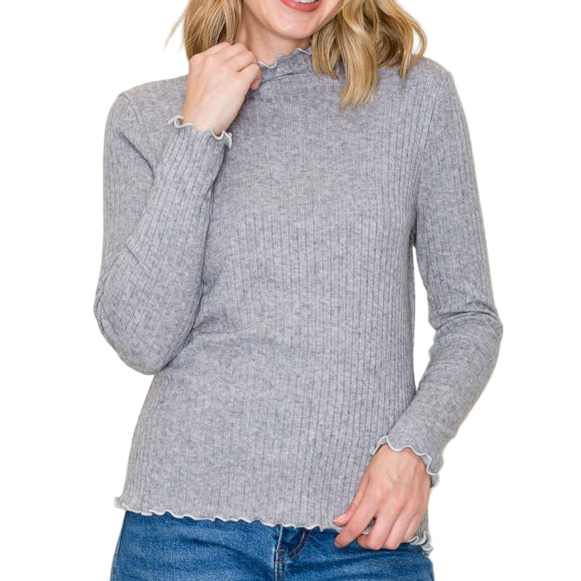 Woman wearing a gray ribbed sweater and blue jeans against a plain background