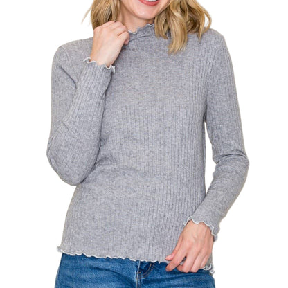 Woman wearing a gray ribbed sweater and blue jeans against a plain background