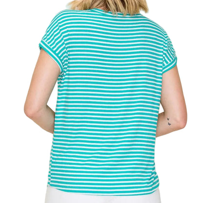 Woman wearing a turquoise and white striped shirt with white shorts on a beige background