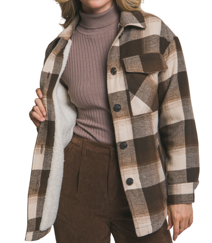 Woman wearing a plaid jacket over a sweater and pants on a plain background