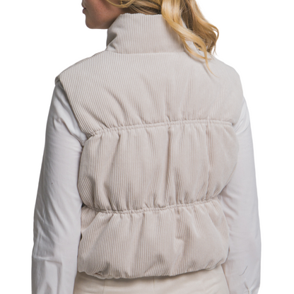 Person wearing a beige puffer vest over a light-colored shirt and skirt on a plain background