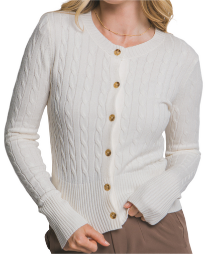 Woman wearing a white cable knit cardigan with gold buttons on a plain background