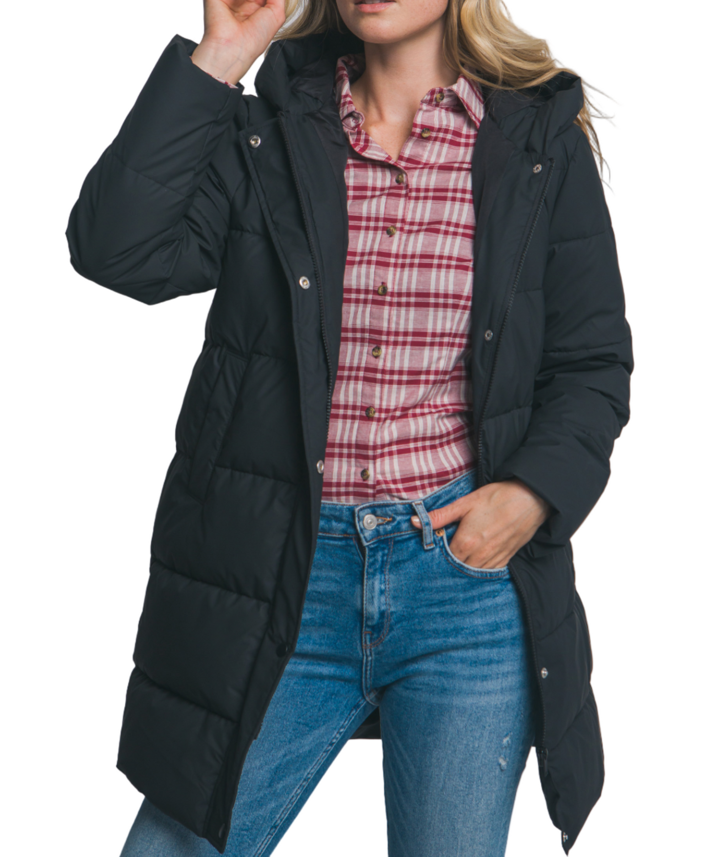 Woman wearing a black puffer coat over a plaid shirt and jeans on a plain background