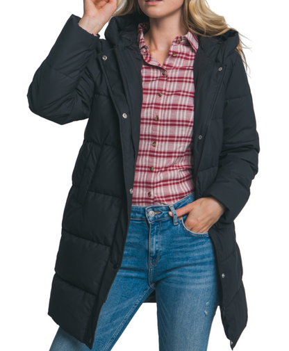 Woman wearing a black puffer coat over a plaid shirt and jeans on a plain background