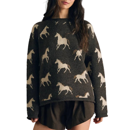 A woman modeling a dark charcoal knit sweater with a repeating cream horse pattern, paired with dark shorts, set against a solid dark red background.