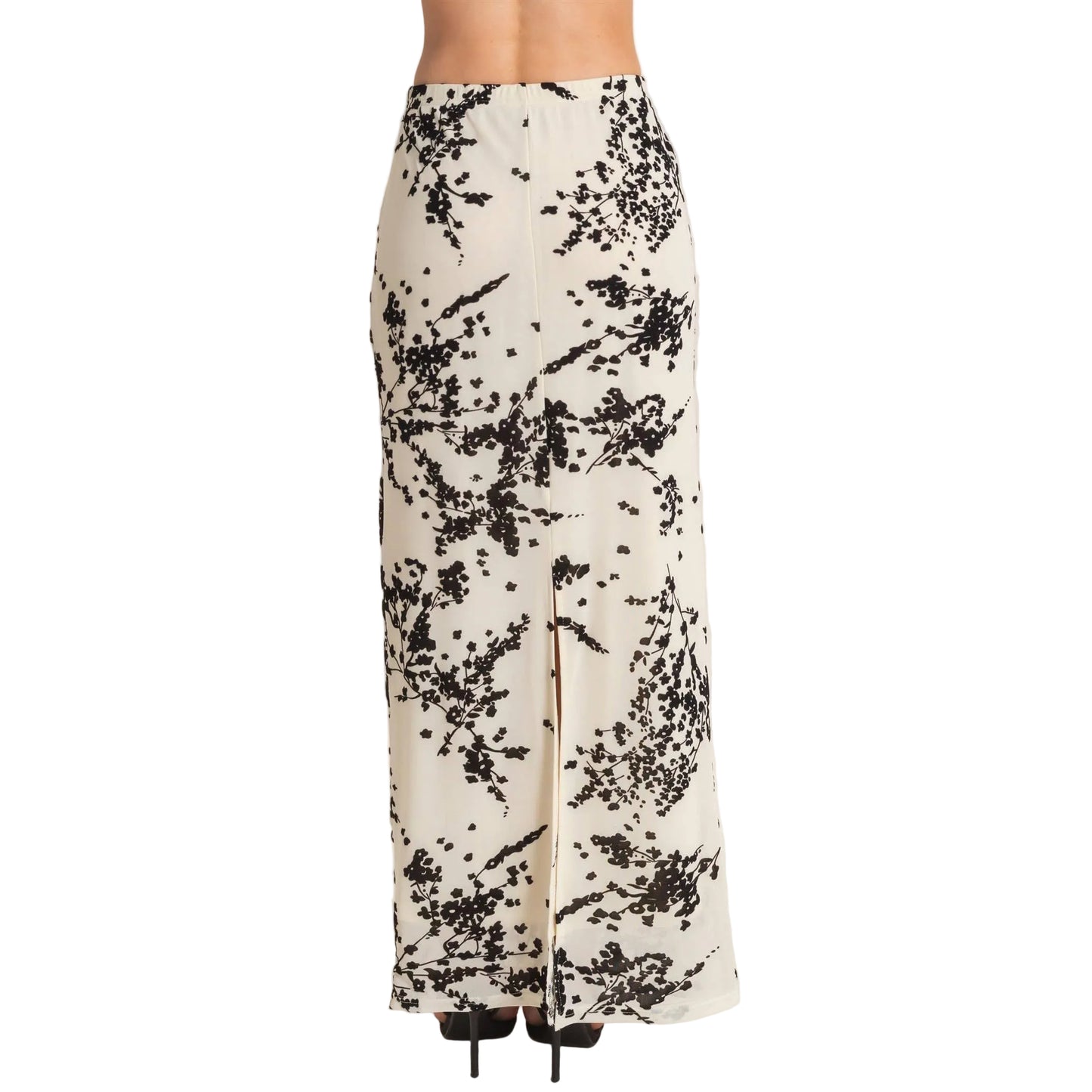 A high-waisted, floor-length maxi skirt with a black abstract floral or brushstroke pattern on a warm cream background, featuring a front slit and worn with black heels.