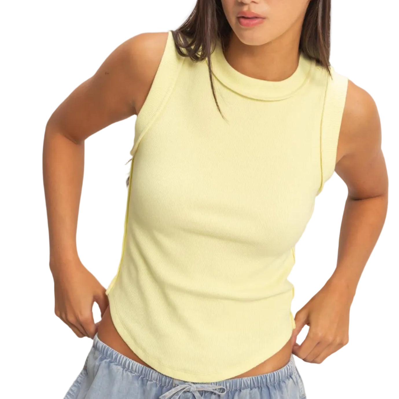 Woman wearing a light yellow sleeveless top and blue pants against a plain background