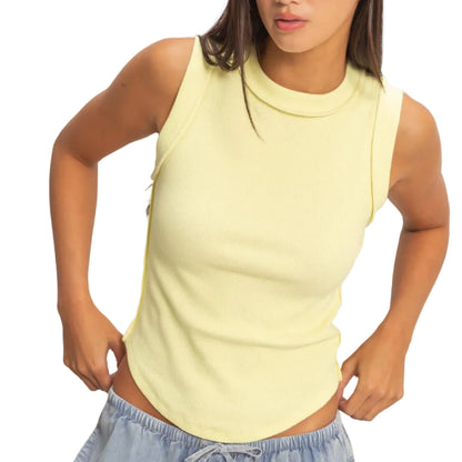 Woman wearing a light yellow sleeveless top and blue pants against a plain background