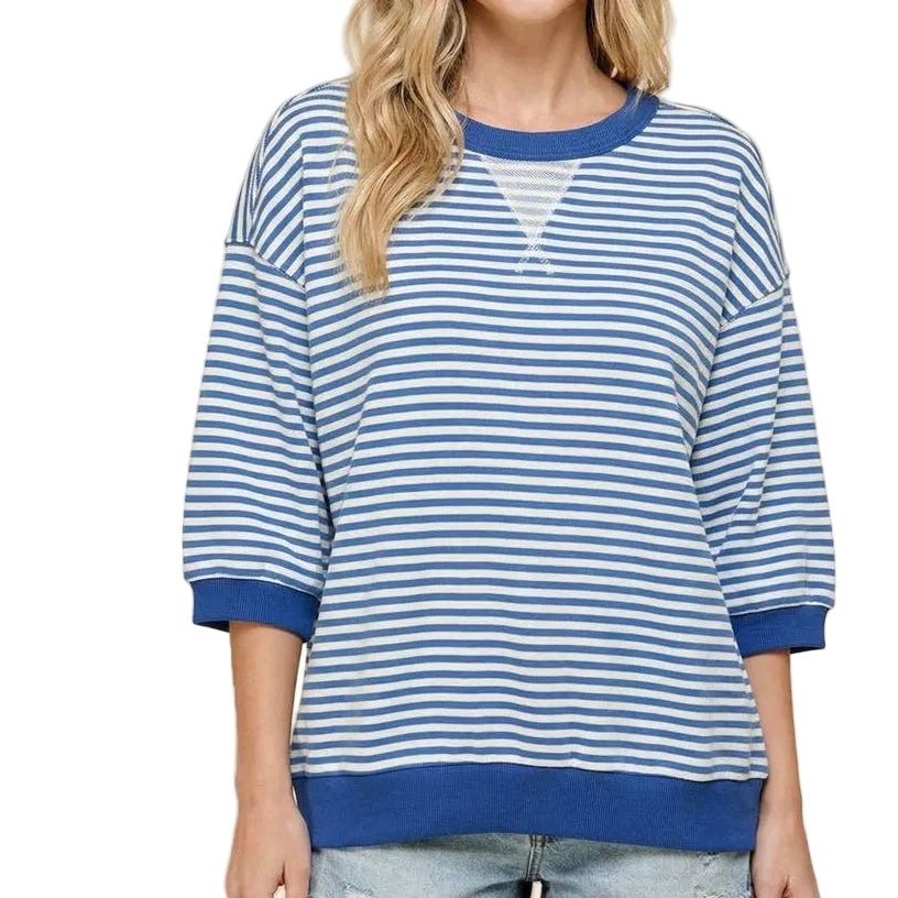 Woman wearing a blue and white striped sweater with denim shorts on a beige background