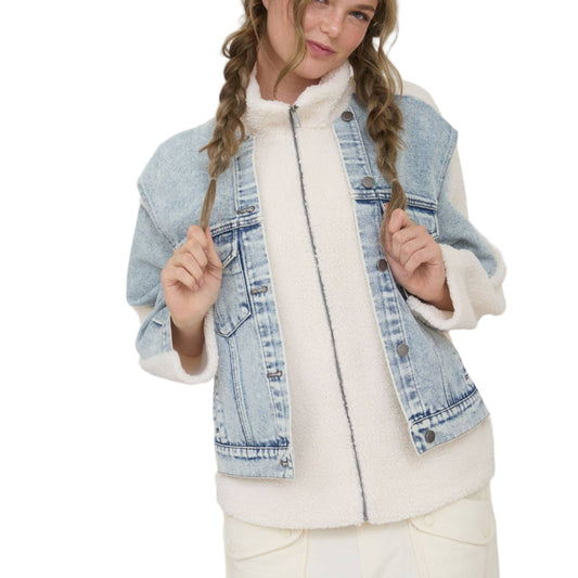 Woman wearing a denim vest over a white outfit against a plain background