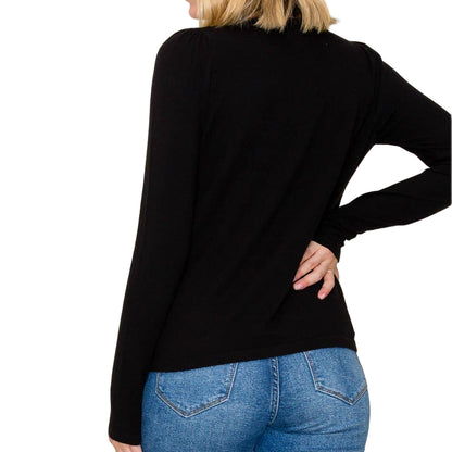 Woman wearing a black sweater and blue jeans against a plain background