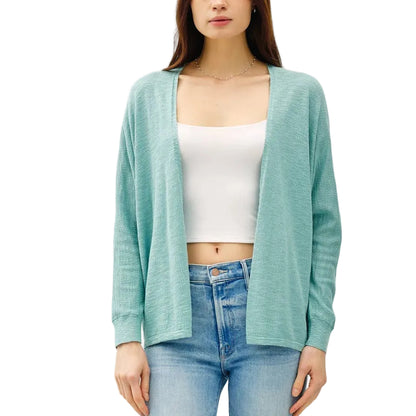 Woman wearing a light blue cardigan, white top, and jeans on a white background