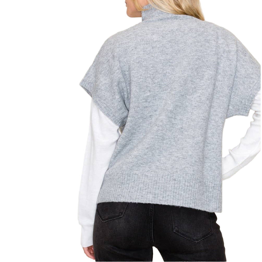 Person wearing a gray poncho over a white shirt and black pants on a beige background
