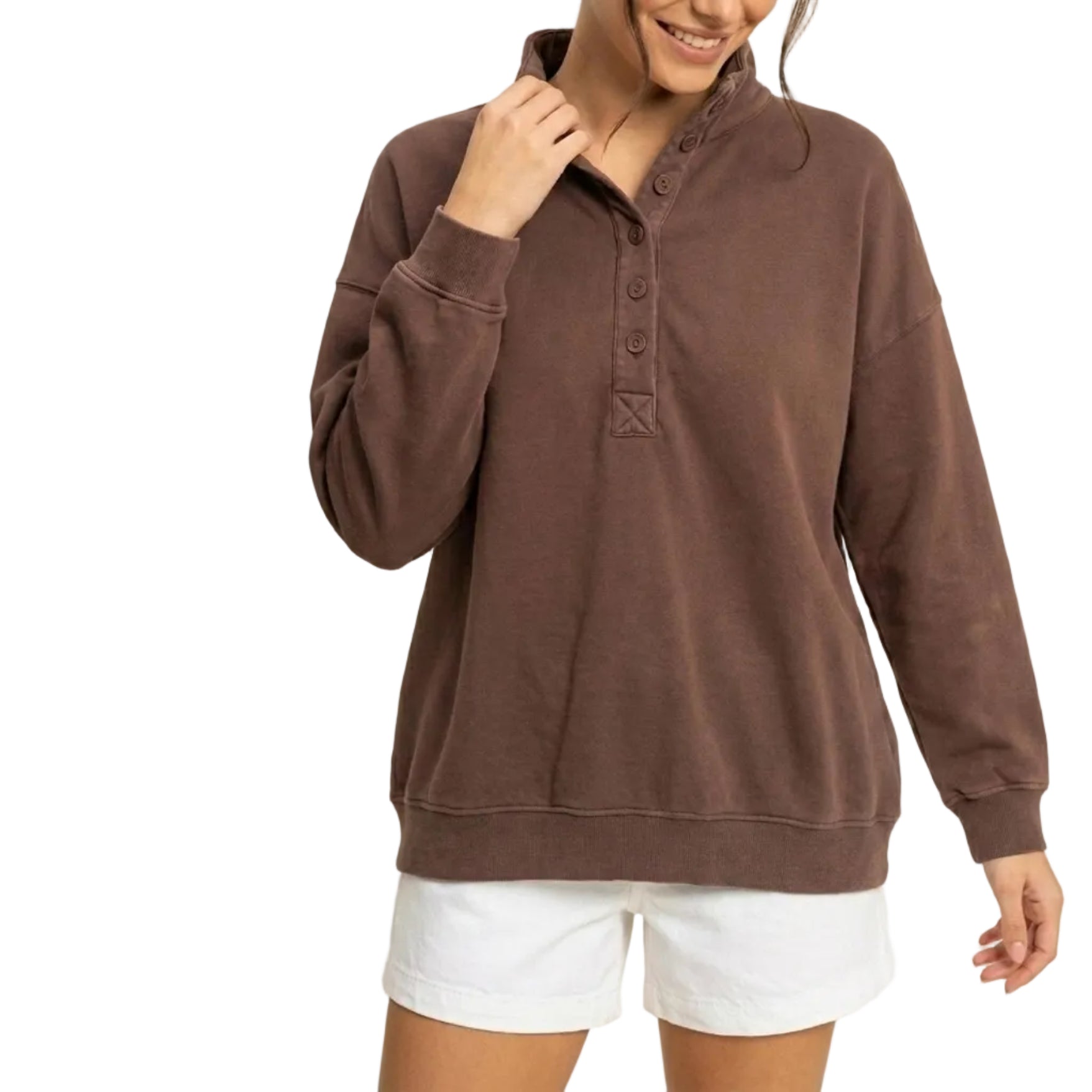 A woman wearing a brown long-sleeve henley sweatshirt with a buttoned collar, paired with white shorts, standing against a plain beige background.