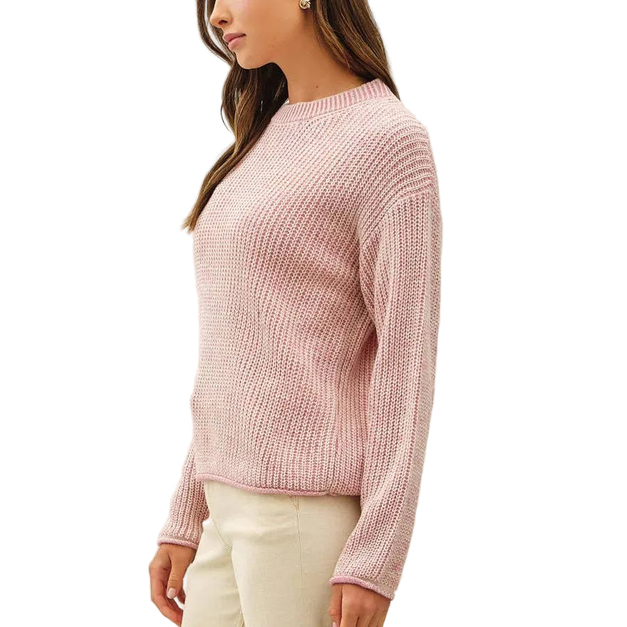 A woman modeling a light pink ribbed knit sweater and cream wide-leg trousers against a plain off-white studio background.