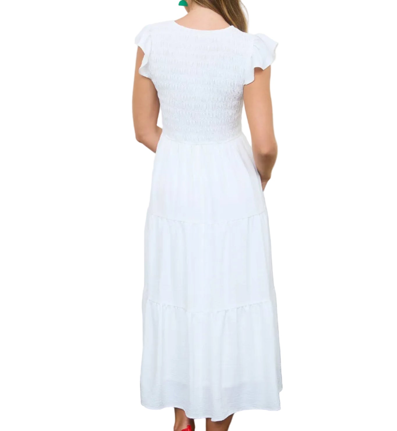 Woman in a white dress standing in a room with wicker baskets and wooden crates.