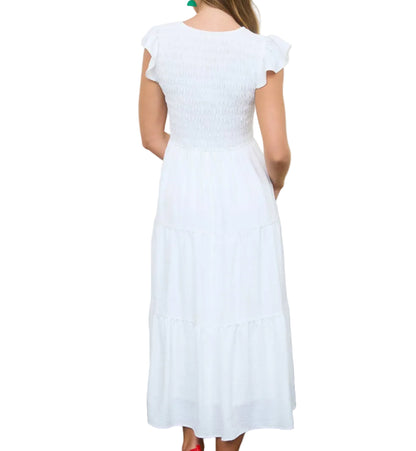 Woman in a white dress standing in a room with wicker baskets and wooden crates.