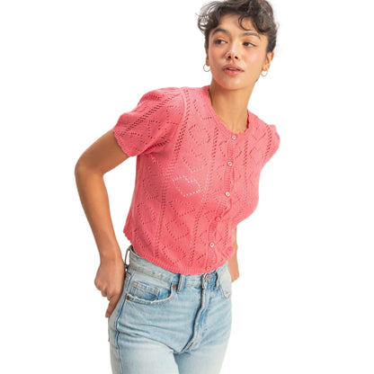 Woman wearing a pink knitted top and light blue jeans against a plain background