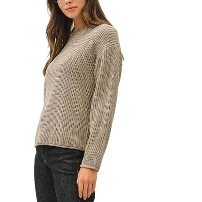 A woman modeling a beige ribbed knit sweater, black jeans, and dark sneakers against a plain white studio background.