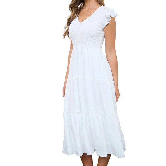 Woman in a white dress standing in a rustic setting with wicker baskets and wooden crates.