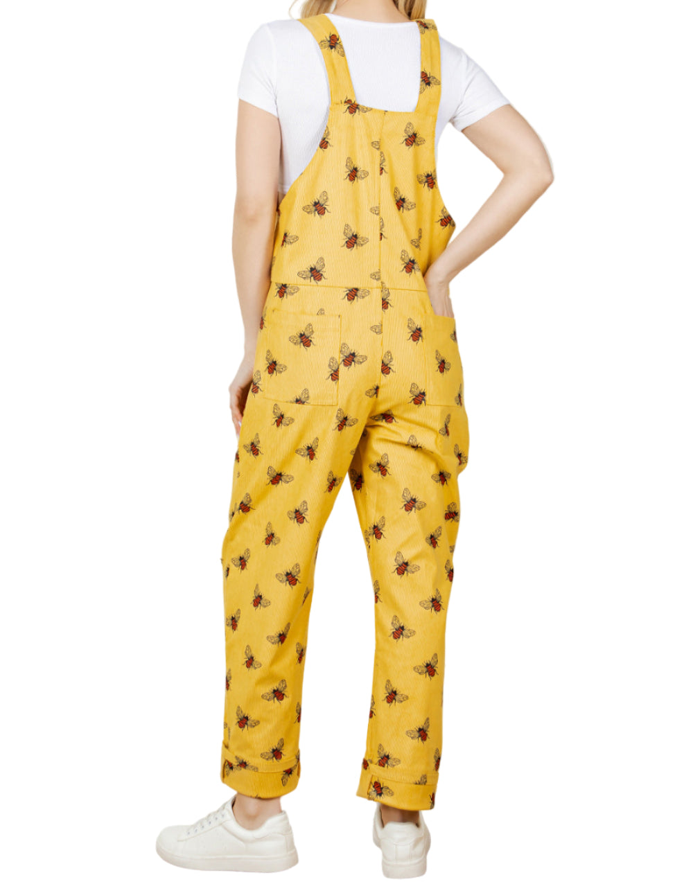 Person wearing yellow floral overalls standing in a room with a plant.