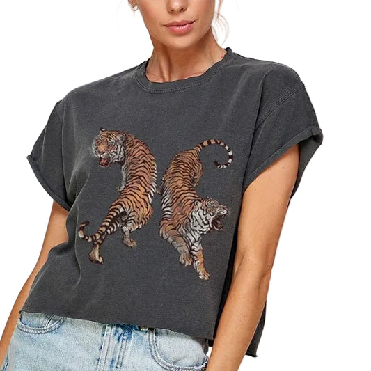 Woman wearing a dark gray t-shirt with tiger designs and light blue denim shorts on a plain background