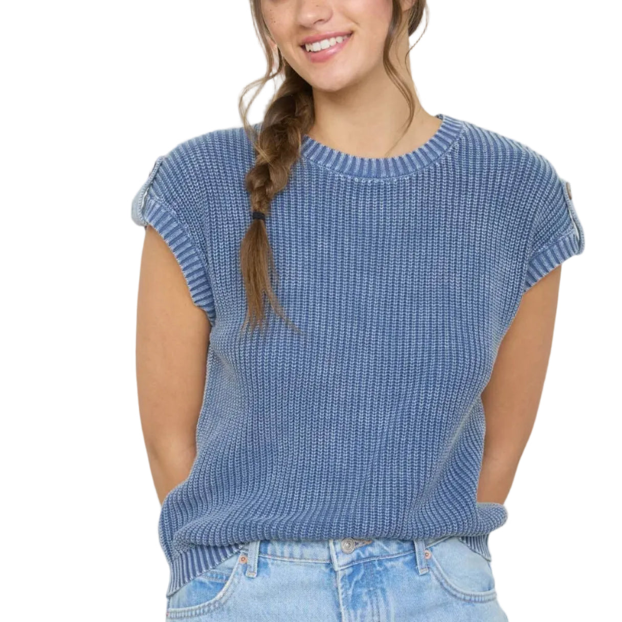 Woman wearing a blue ribbed sweater and light blue jeans standing against a white wall with framed pictures.