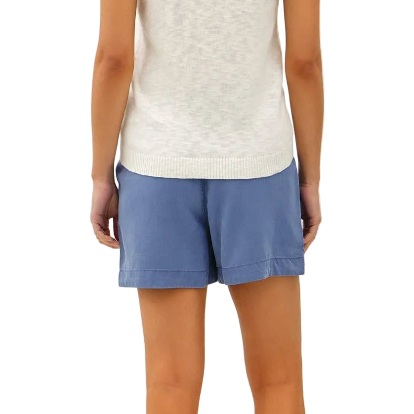 Woman wearing a white lace top and blue shorts on a plain background