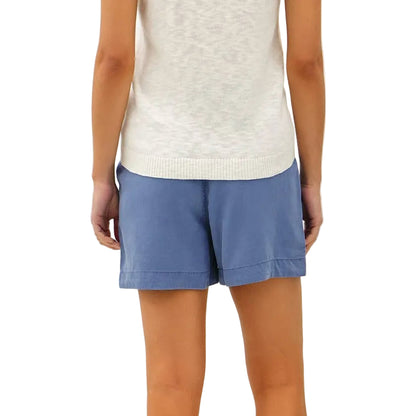 Woman wearing a white lace top and blue shorts on a plain background