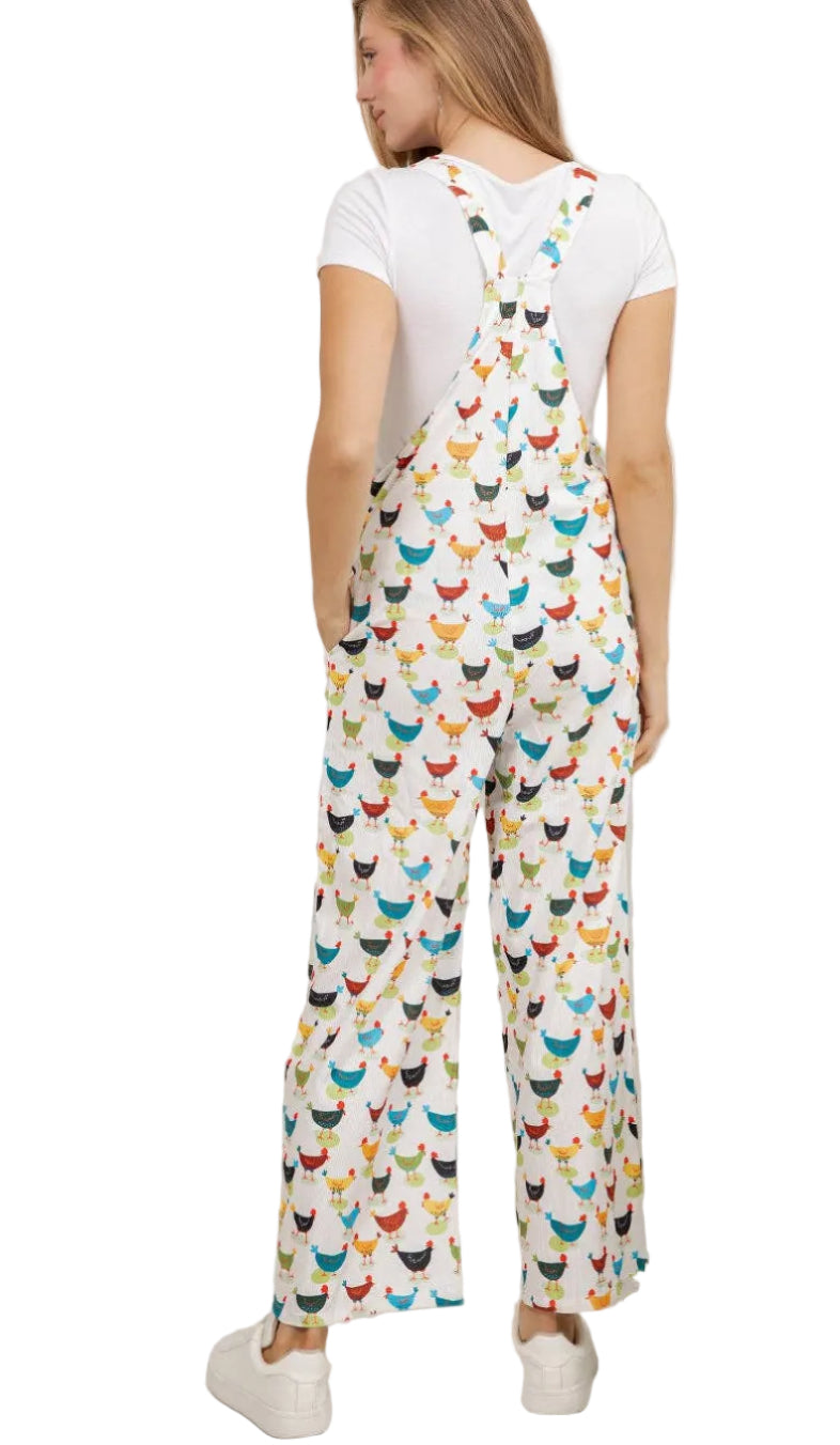 Woman wearing a colorful chicken-patterned jumpsuit in a room with plants.