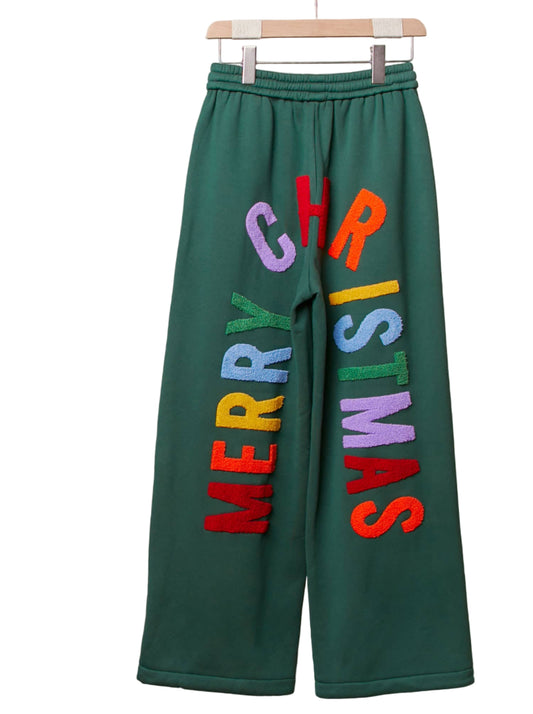Green sweatpants with colorful 'Merry Christmas' text on a wooden hanger.
