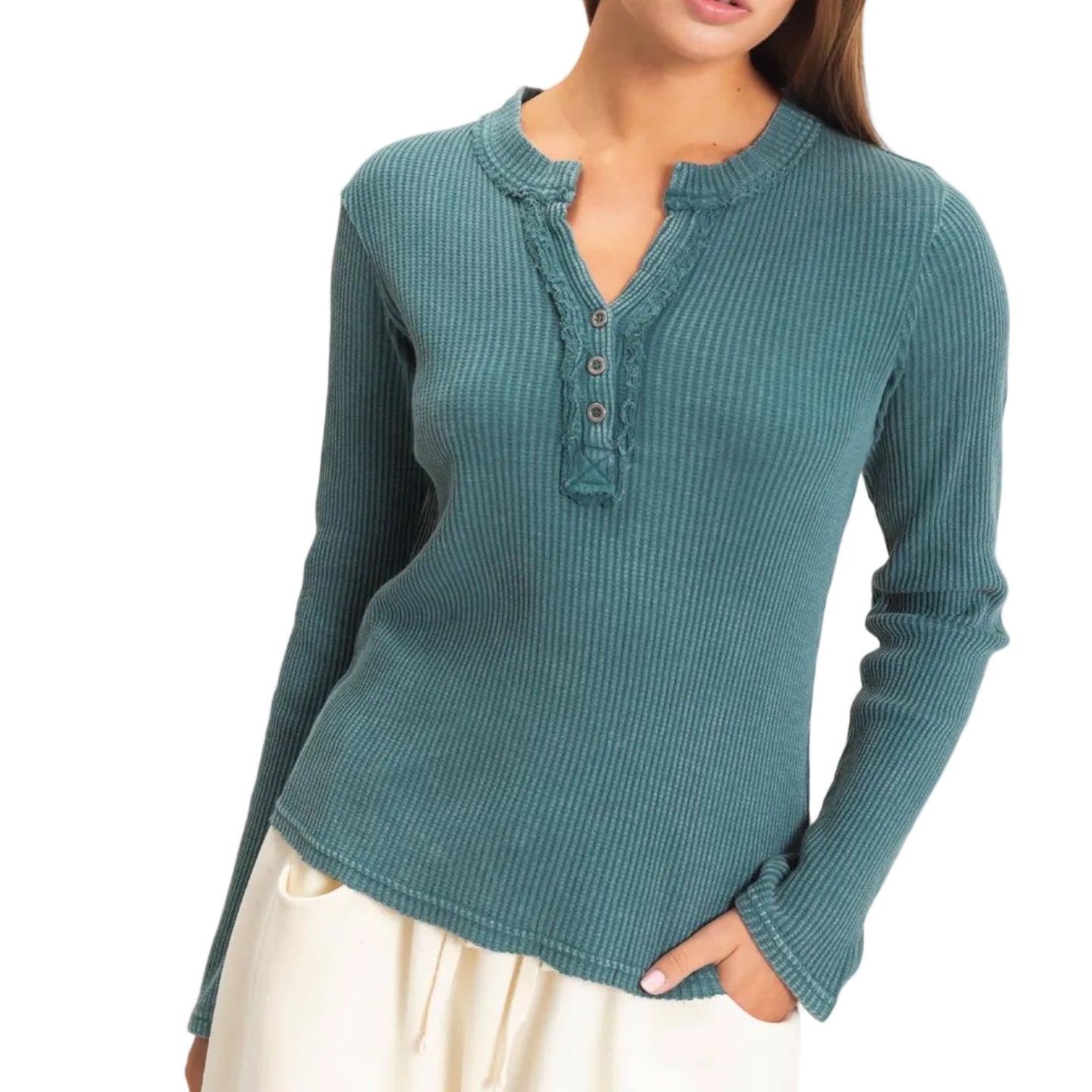 A woman wearing a teal ribbed long-sleeve henley top with a button placket, paired with cream pants, standing against a plain light beige background.