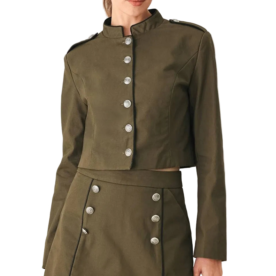 A woman modeling a matching olive green cropped jacket and high-waisted mini skirt set with silver-tone buttons, photographed against a plain light gray studio background.