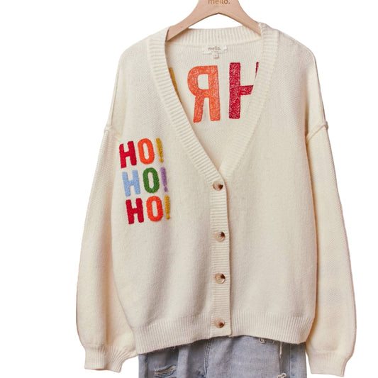 White cardigan with colorful text on a hanger against a neutral wall.