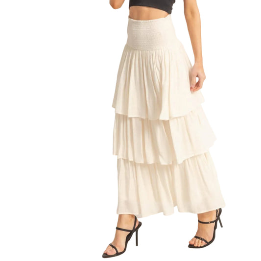 Woman wearing a black top and white tiered skirt on a plain background