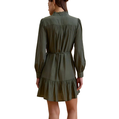 A woman viewed from the back wearing an olive green long-sleeve mini dress with a gathered waist and ruffled hem, paired with black ankle boots, against a solid beige studio background.