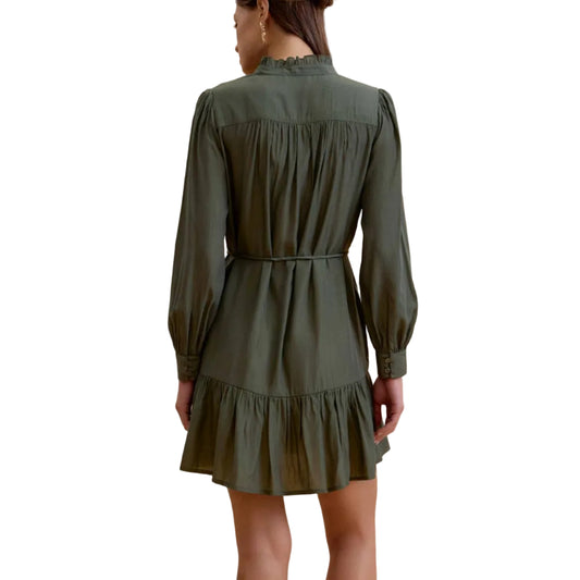 A woman viewed from the back wearing an olive green long-sleeve mini dress with a gathered waist and ruffled hem, paired with black ankle boots, against a solid beige studio background.