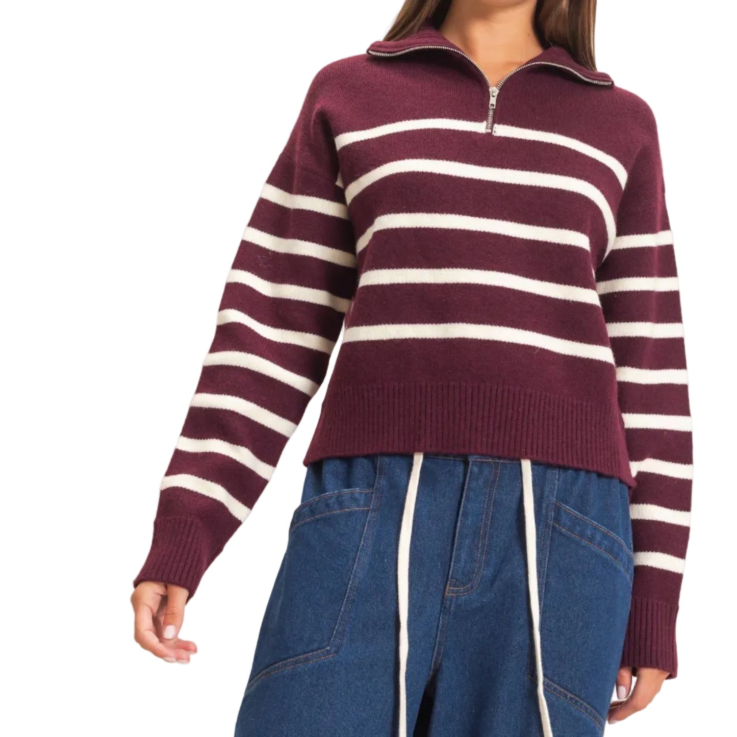 A woman wearing a burgundy and cream striped half-zip knit sweater with blue wide-leg pants, standing against a plain light beige background.