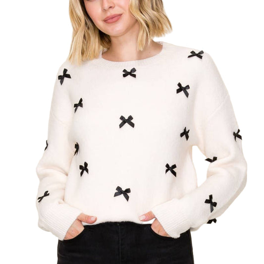 Woman wearing a white sweater with black bow patterns against a plain background