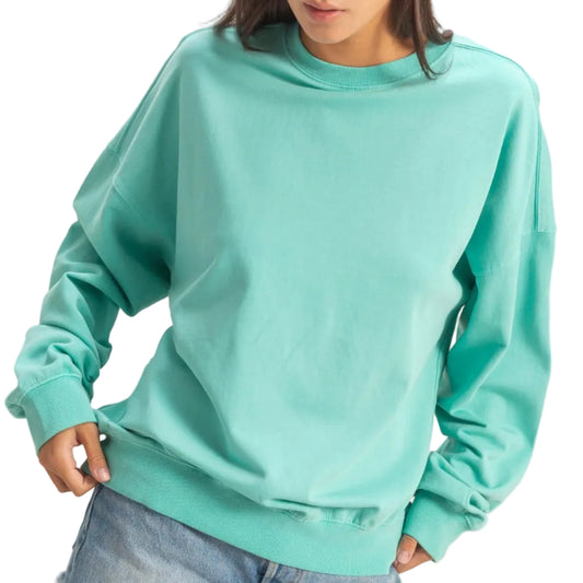 Woman wearing a teal sweatshirt and denim shorts on a plain background