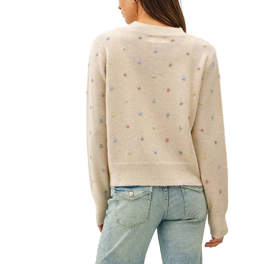 A woman shown from the back wearing a cream knit sweater with tiny multicolored embroidered dots and light-wash blue flare jeans, standing against a plain white studio background.