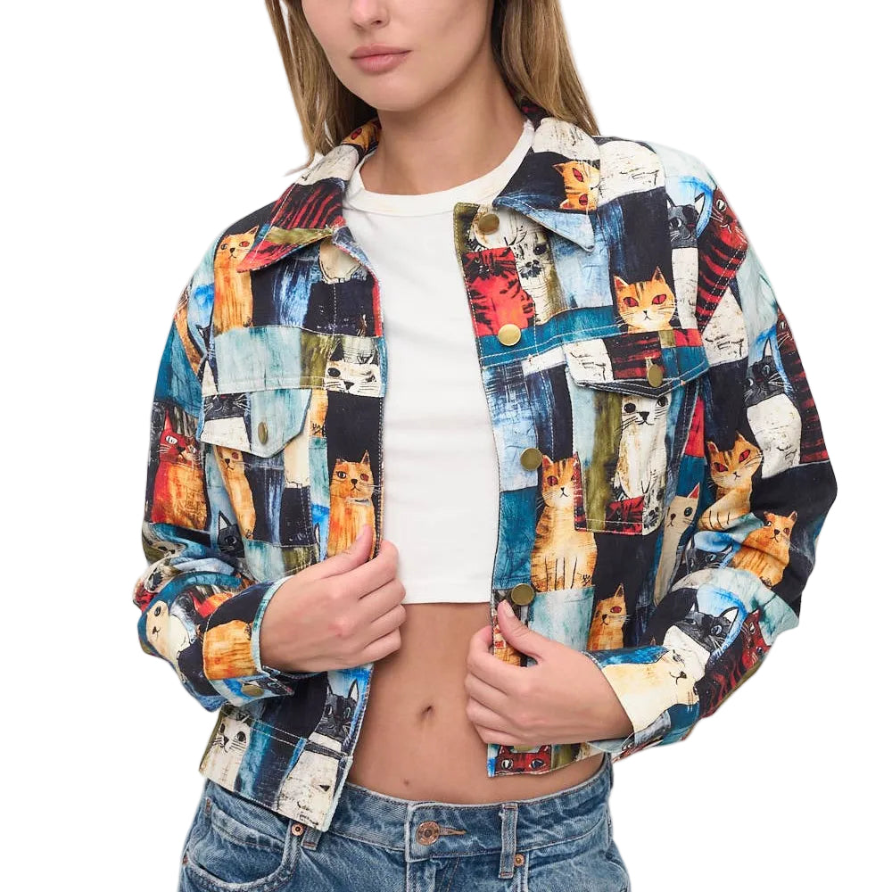 A woman modeling a cropped button-up jacket covered in a colorful collage print of various cats, worn over a white crop top and blue jeans against a plain white background.