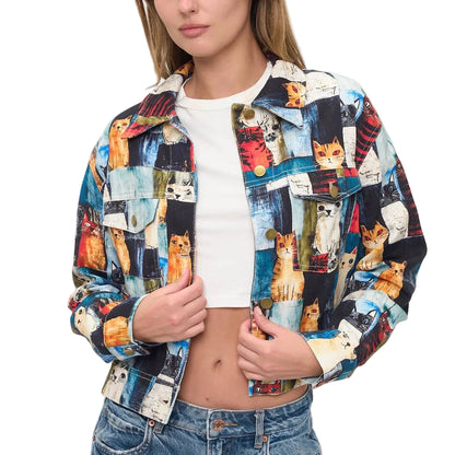 A woman modeling a cropped button-up jacket covered in a colorful collage print of various cats, worn over a white crop top and blue jeans against a plain white background.