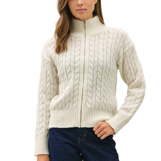 Woman wearing a white cable knit sweater and dark blue jeans on a white background