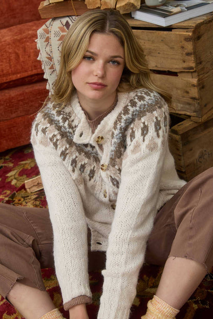 Woman wearing a patterned sweater sitting on a wooden floor.