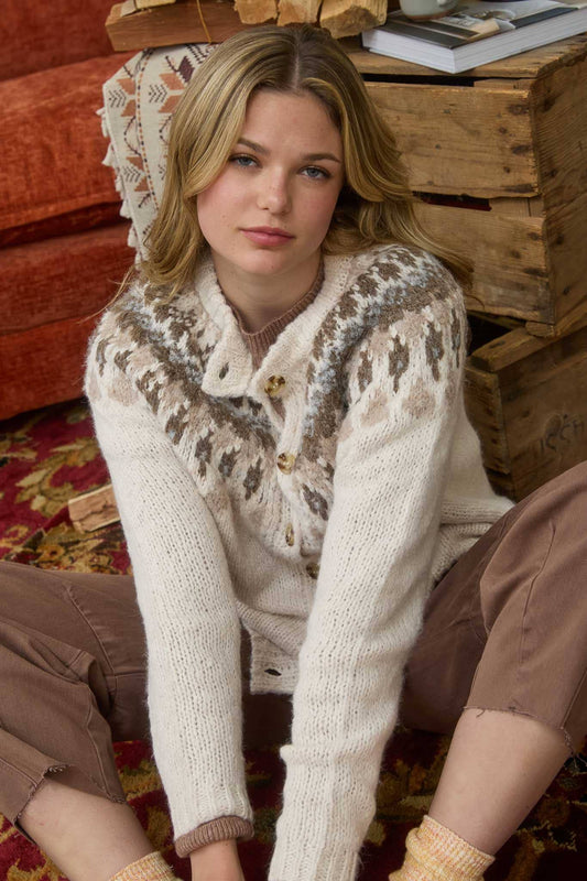 Woman wearing a patterned sweater sitting on a wooden floor.
