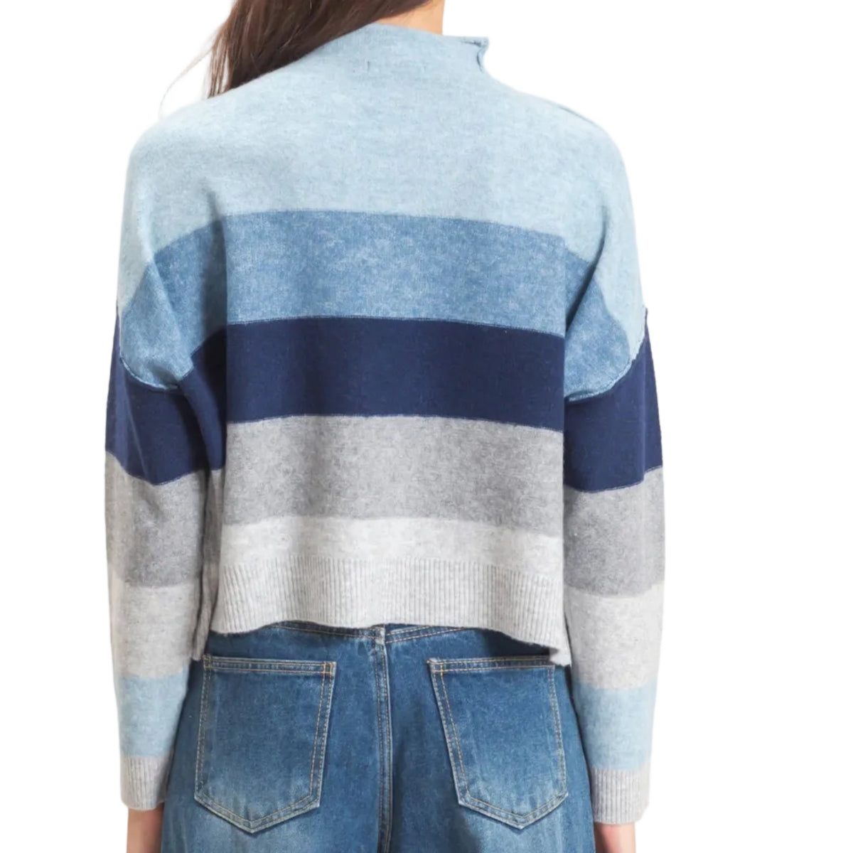 A woman viewed from the back wearing a cropped mock-neck knit sweater with horizontal stripes in light blue, navy, gray, and white, paired with blue jeans against a plain light background.