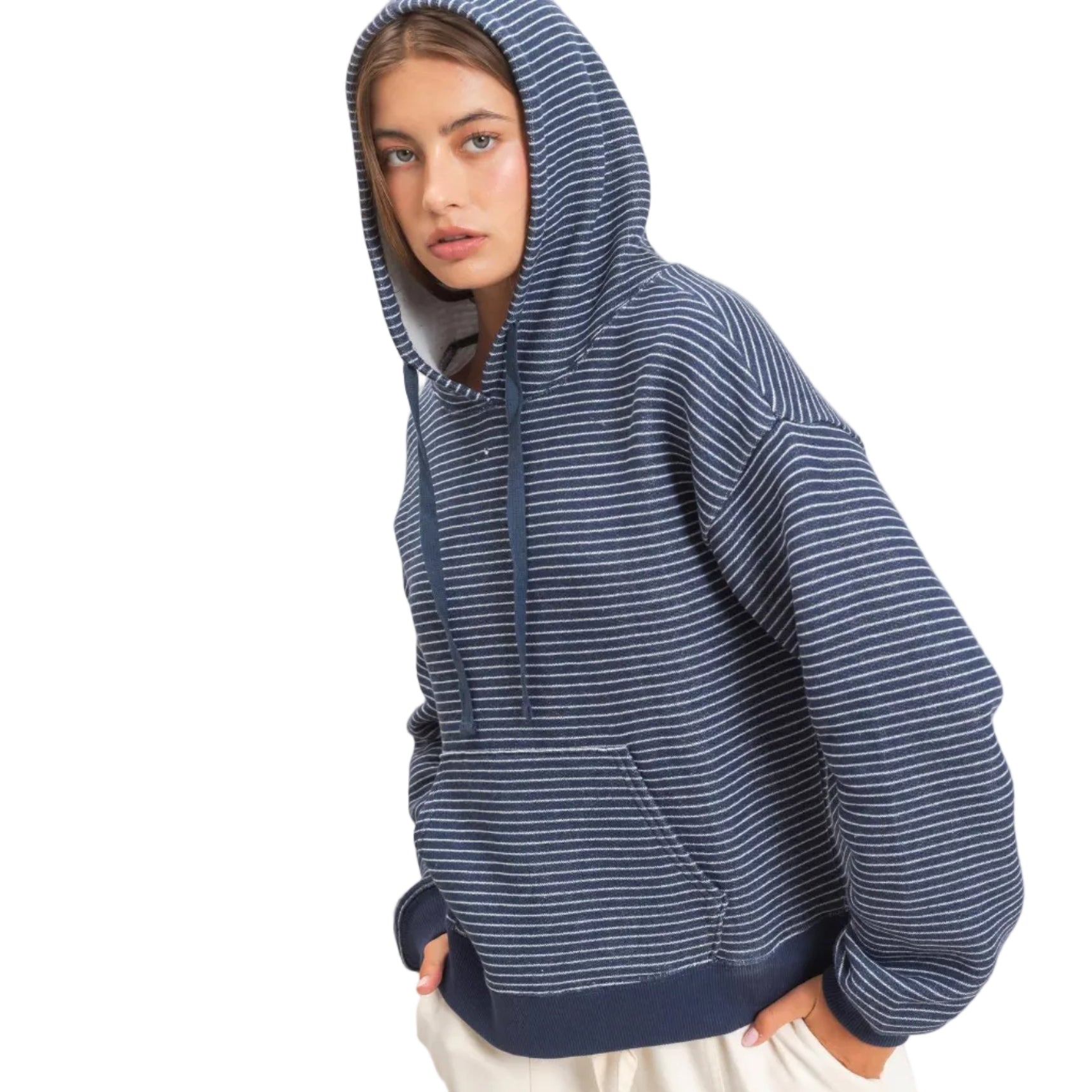 A woman wearing a navy blue and white striped pullover hoodie with a front kangaroo pocket, paired with off-white sweatpants, against a plain beige studio background.