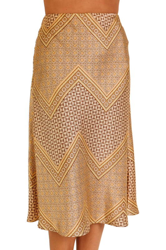 A knee-length skirt with a geometric and chevron pattern in tan, beige, and brown, shown on a model against a plain beige background.