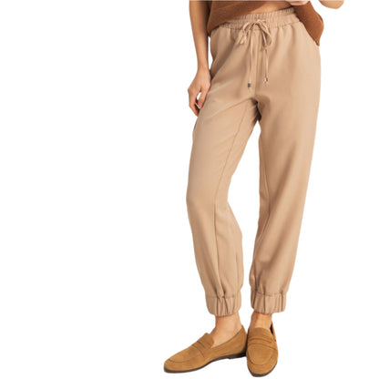 Woman wearing a brown top and beige pants against a white background